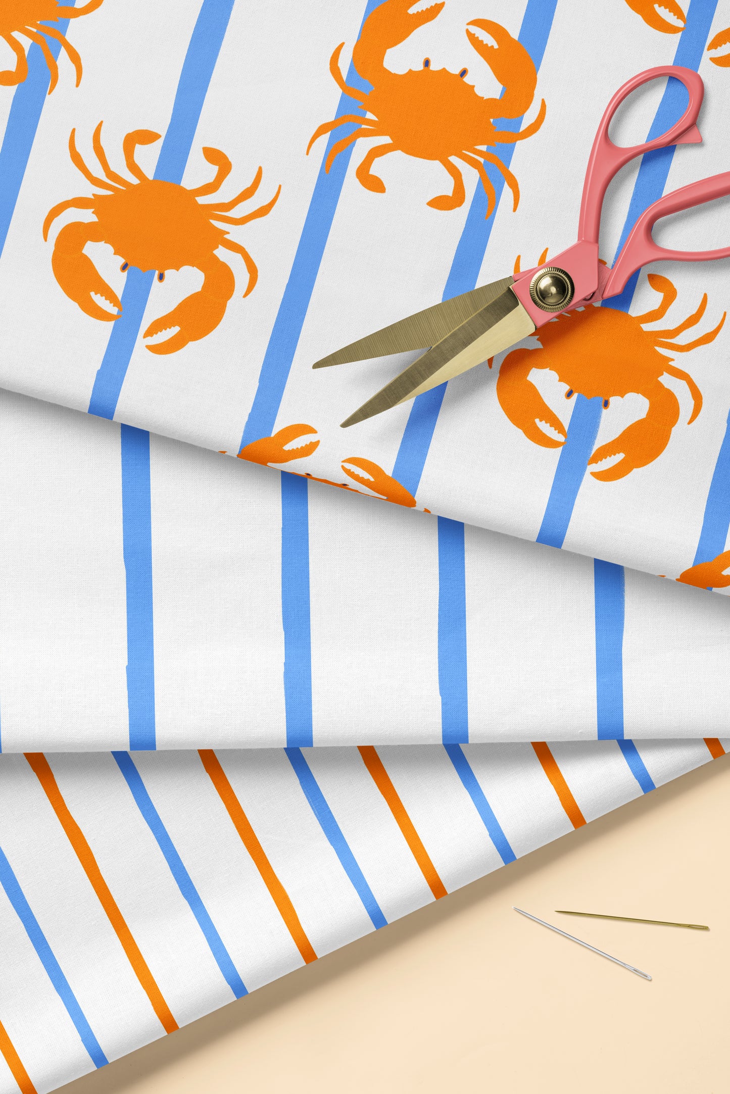 Fabric with orange crabs and blue stripes, scissors on top, on a beige surface