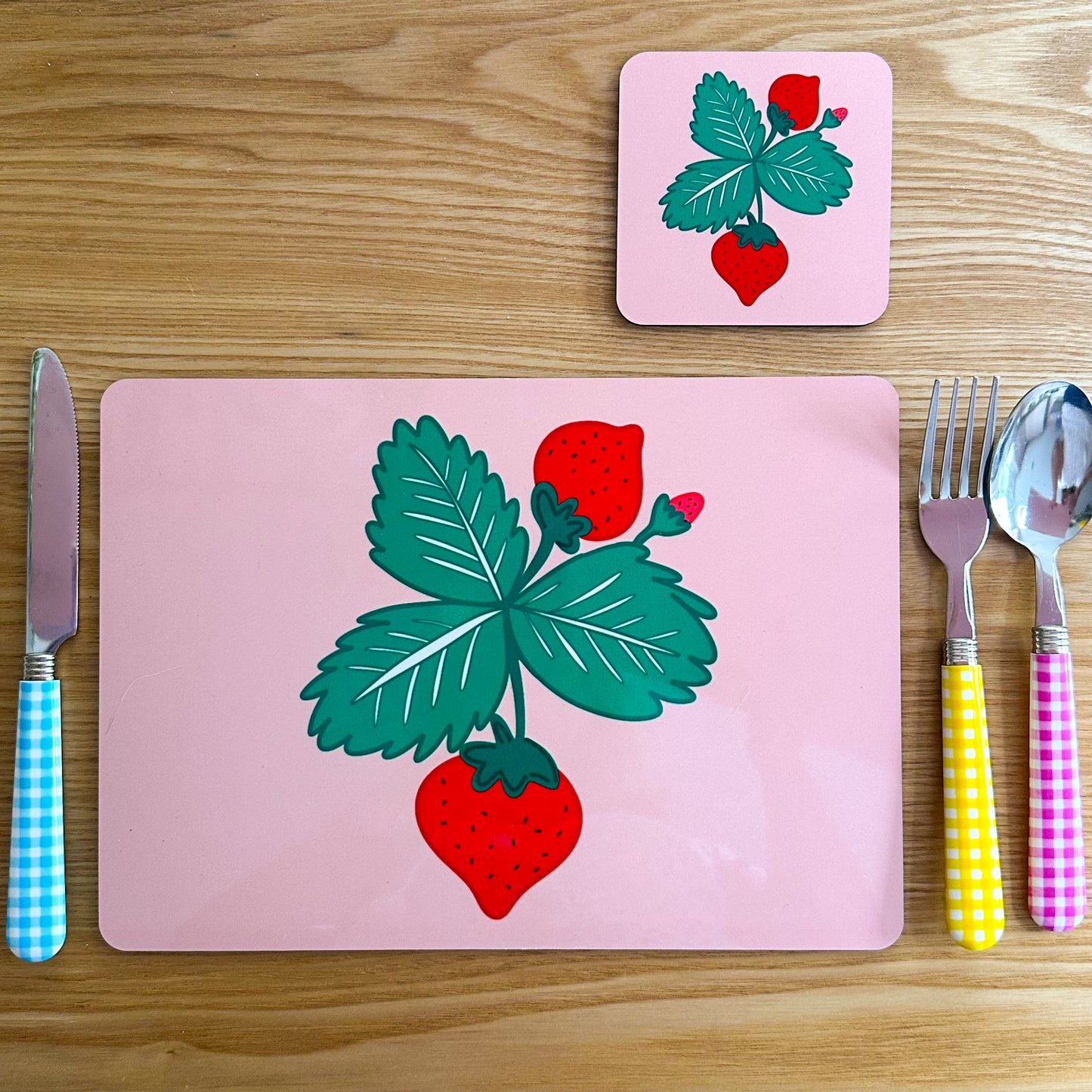 Placemat, coaster, and cutlery set with strawberry design on a wooden surface