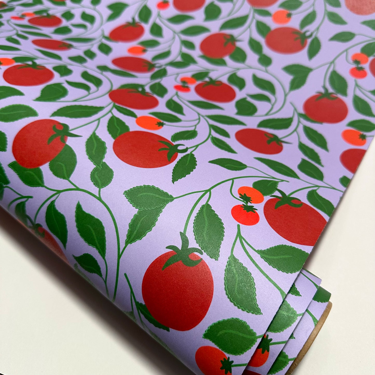 Roll of wallpaper with red tomato and green leaf pattern on a light purple background