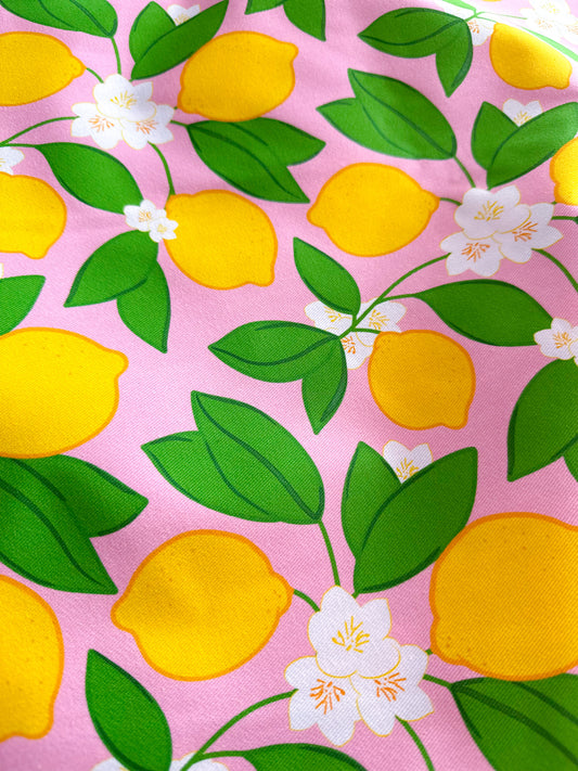 Fabric with lemons, green leaves, and white flowers on a pink background