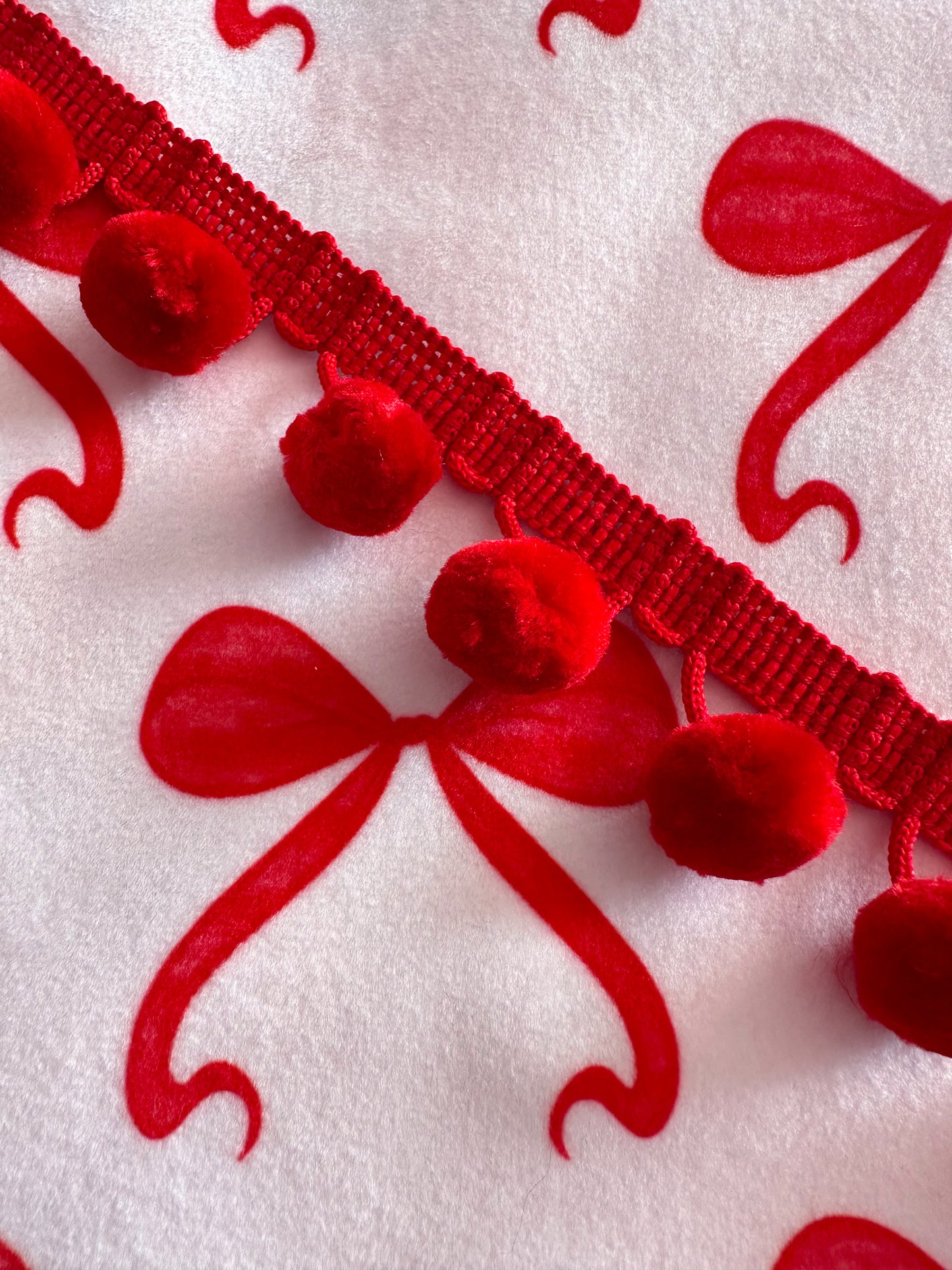 Close-up of red decorative trim with pom-poms and bows velvet fabric