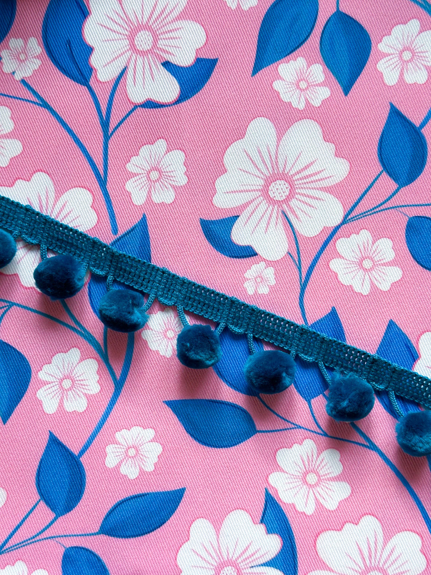 Blue pom-pom trim on a pink fabric with floral and leaf pattern