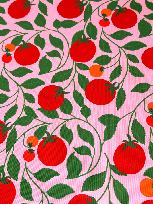 Upholstery sewing fabric with pattern of red tomatoes and green leaves on a pink background